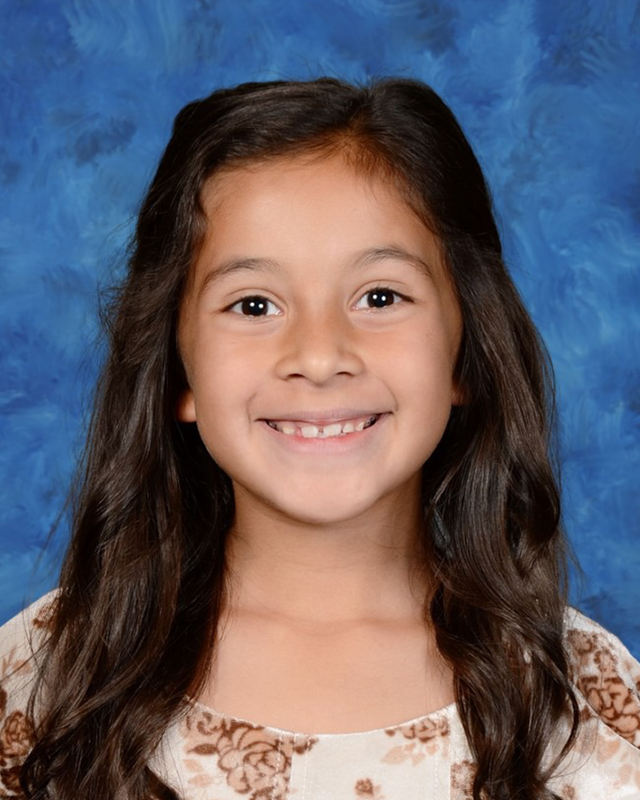 A young girl with long brown hair smiles at the camera.