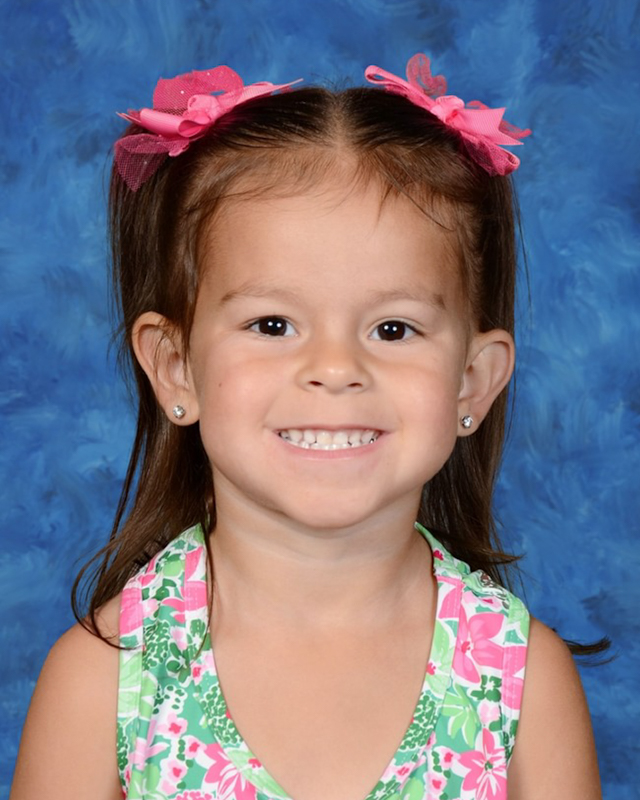 A young girl with pigtails and pink bows smiles at the camera.