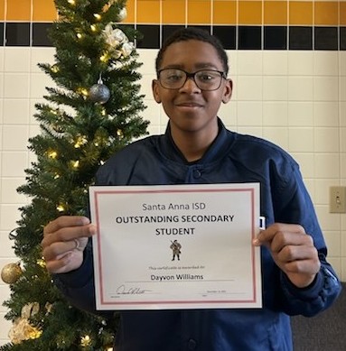 A young man smiles, holding an award in front of a decorated tree.