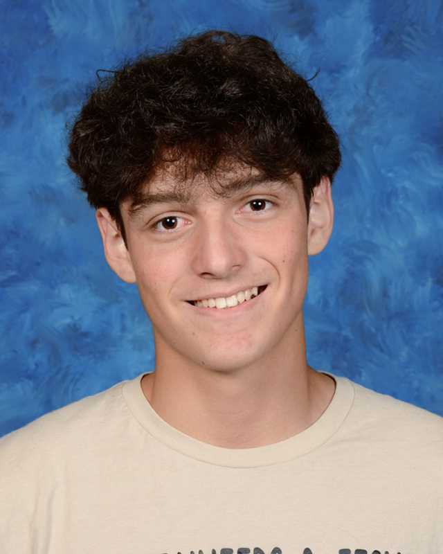A young man with dark, curly hair smiles at the camera.