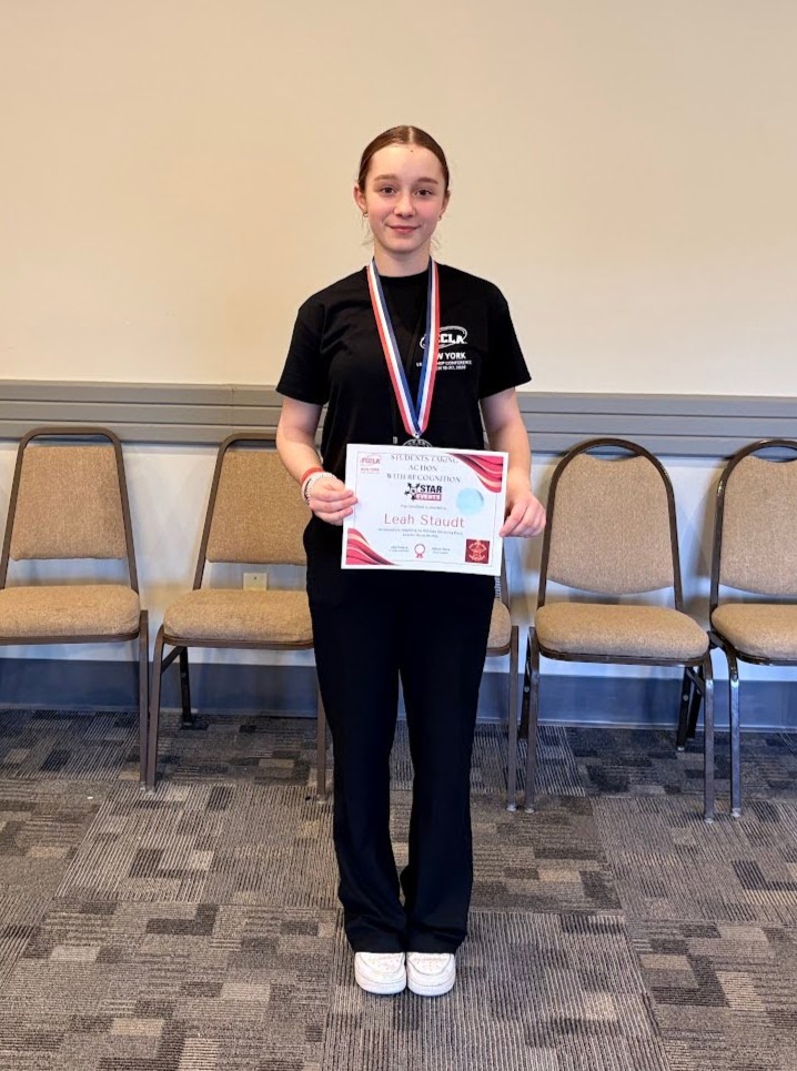 A young woman stands proudly, holding a certificate and wearing a medal.