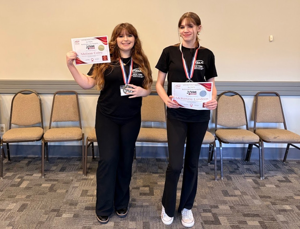 Two young women stand proudly, holding certificates and wearing medals.