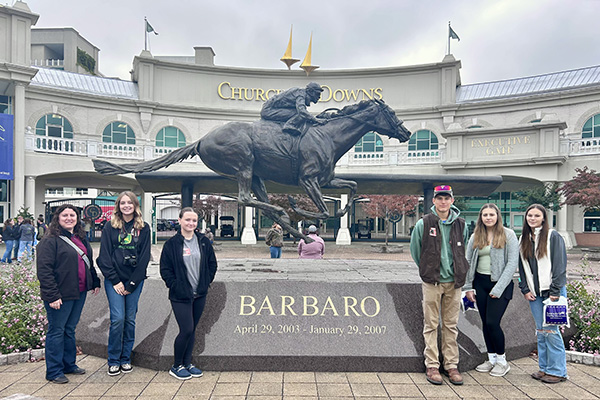 A group of people pose in front of a horse statue and building.