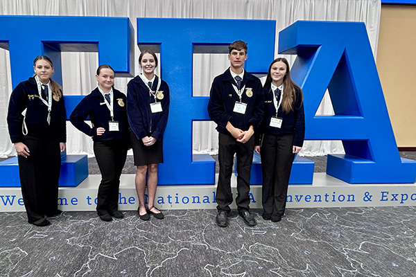 Five young adults pose in front of a large blue FFA sign.