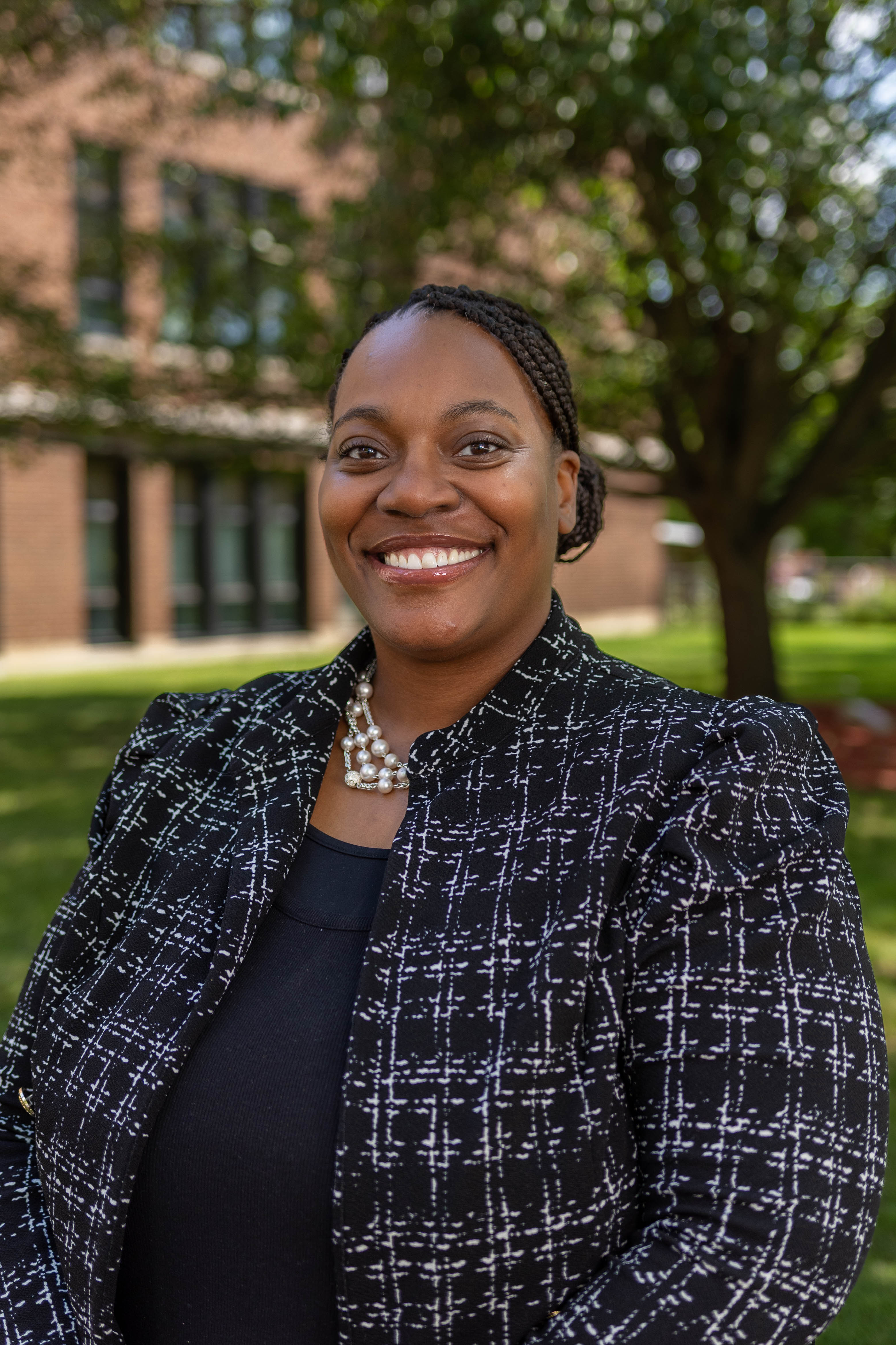 A woman with a warm smile is wearing a black top and a black and white blazer.