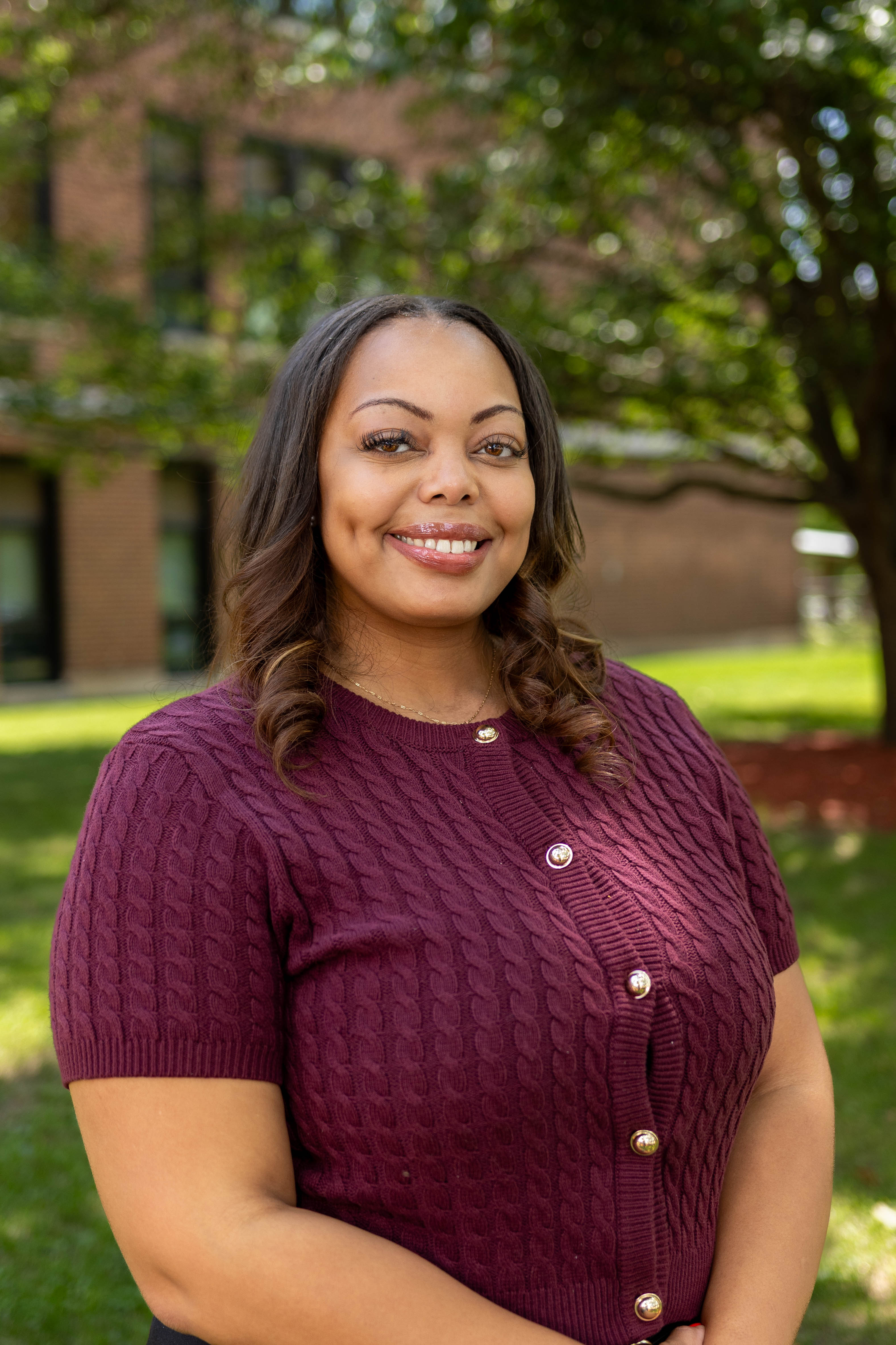 A woman with a warm smile poses outdoors, wearing a burgundy sweater.