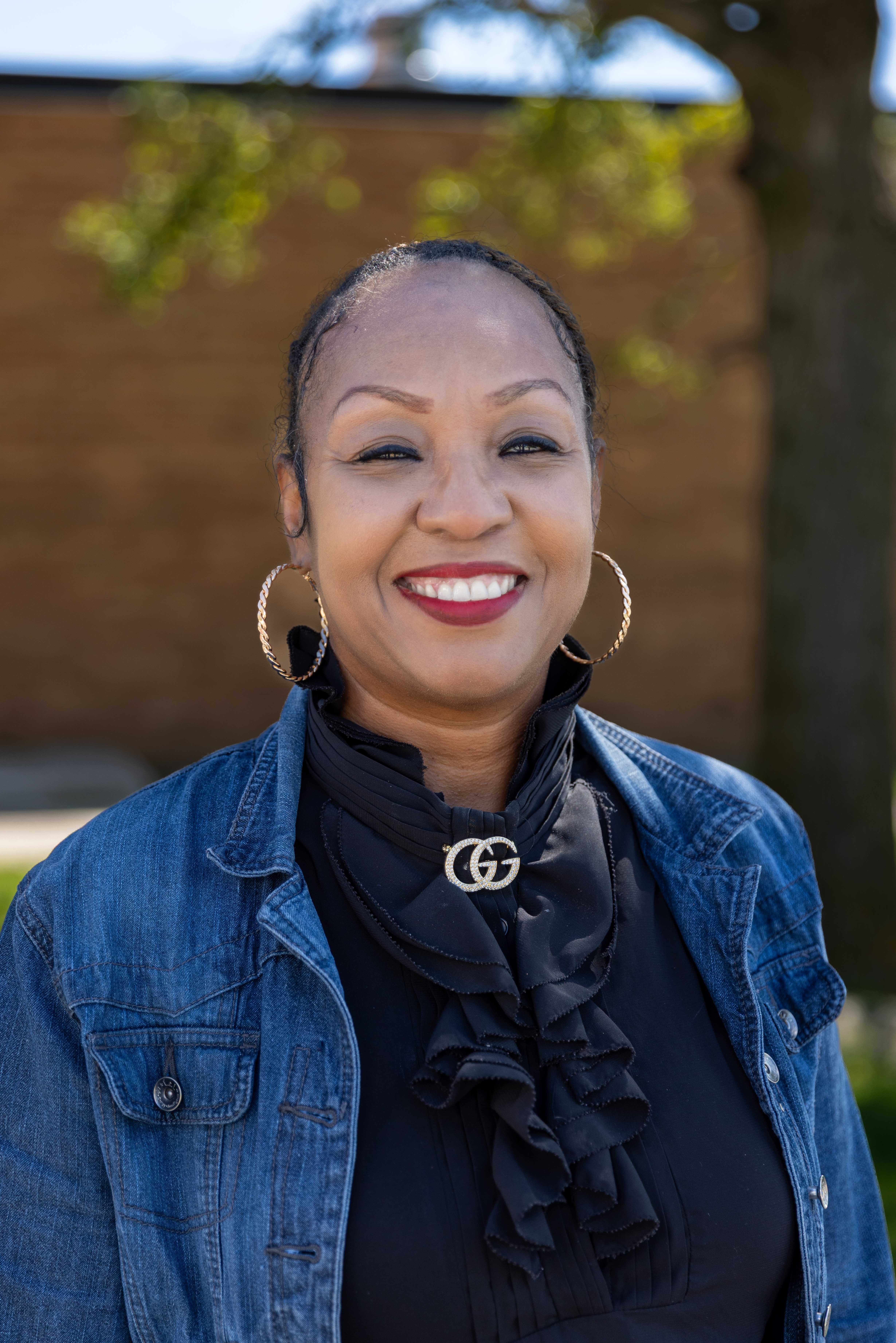 A woman with a warm smile poses outdoors, wearing a denim jacket.