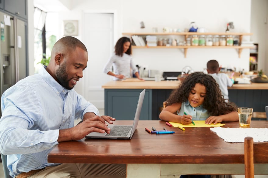 Family sitting at home while husband works on computer