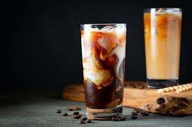 tall cool glass of cold brew coffee with a spash of milk gently swirling down into the drink