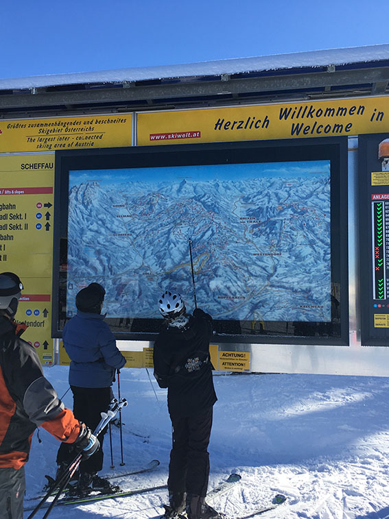Skiers in front of a large panorama map board.
