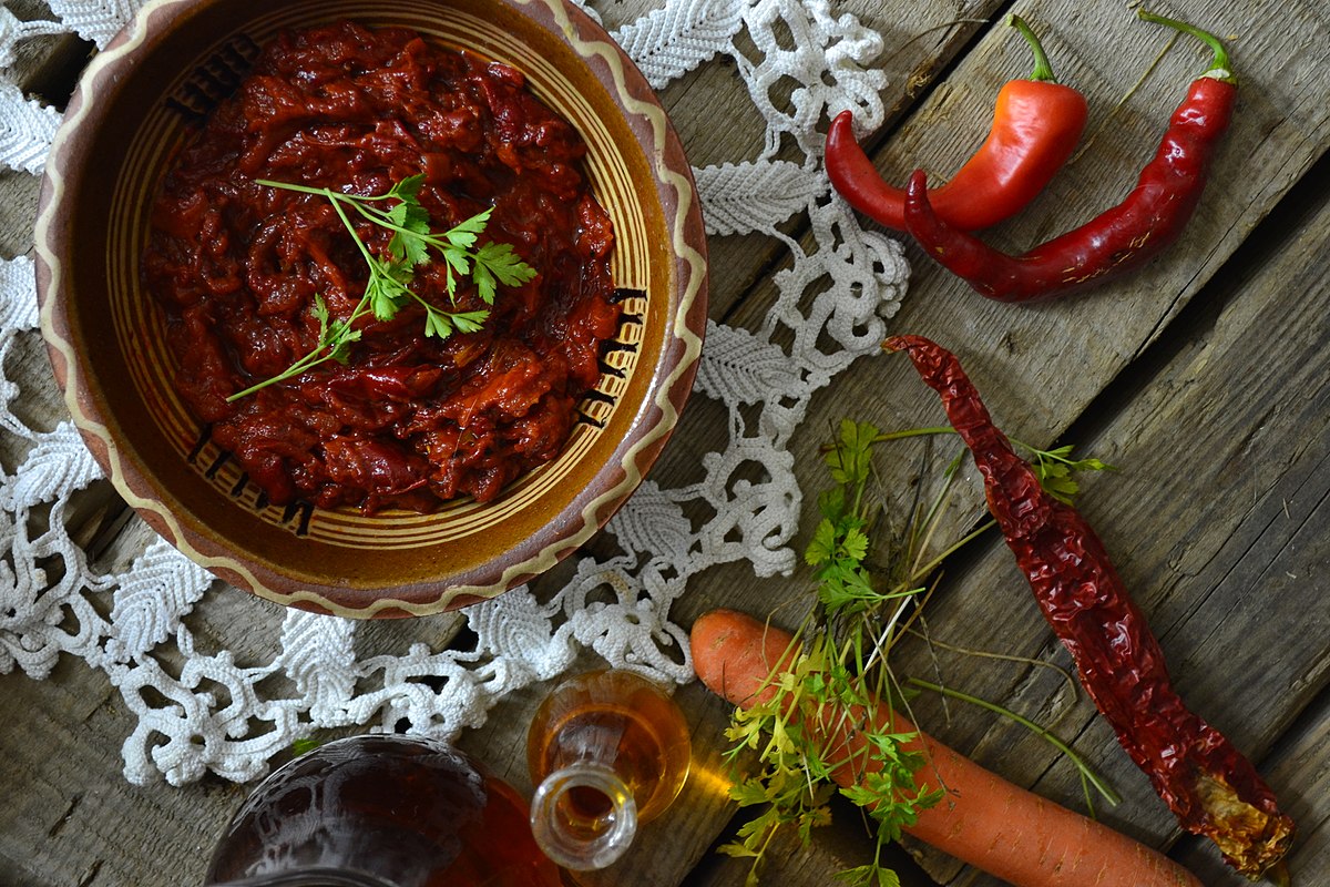 bowl with lyutenica chutney on a wooden table with vegetables