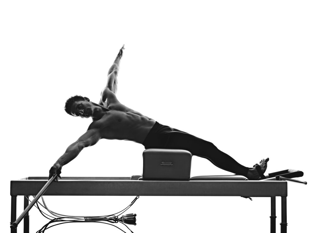 Man laying on long box on reformer doing side stretches while on long box