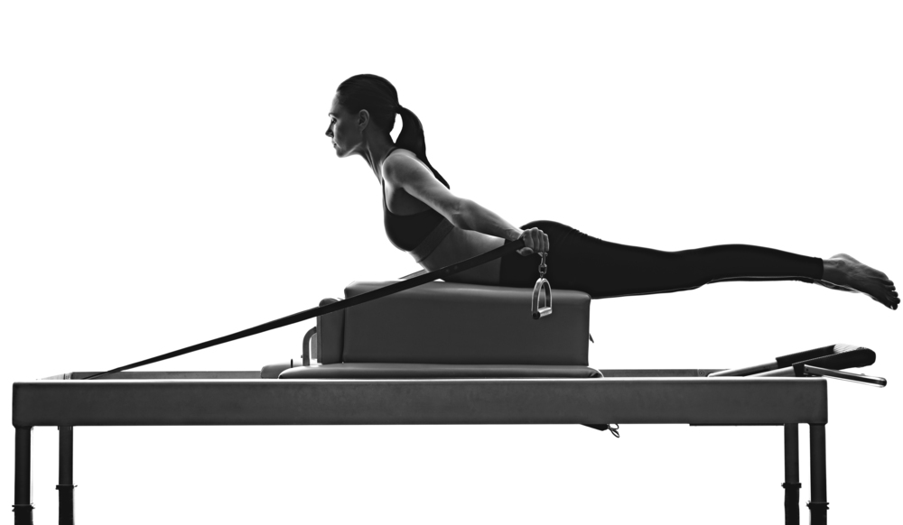 Woman laying on her stomach on the long box on the reformer doing arms with the leg straps