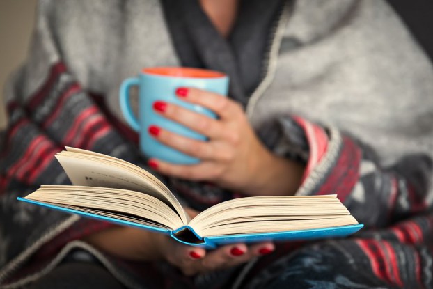 A person in a cozy blanket with a mug of coffee reading a book