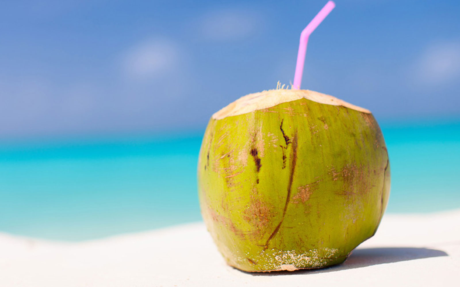 close up of coconut water on the beach with a straw