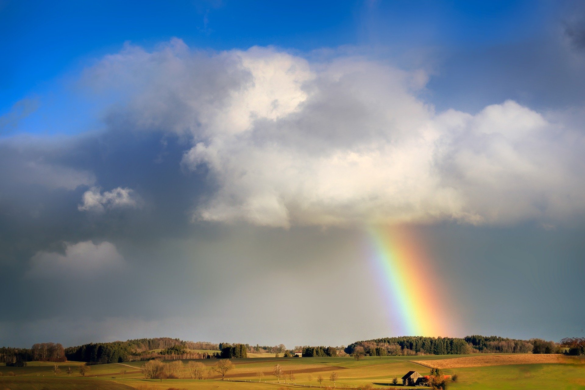 a rainbow in a cloudy sky in a field with some trees and a tiny house
