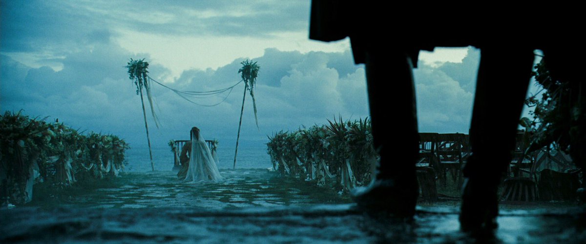 a besodden bride watches a storm roll through, unaware of the man standing behind her