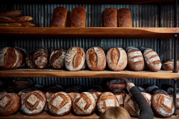 Baker reaching hand to pick a bread loaf amongst many bread loaves
      displayed on shelving
