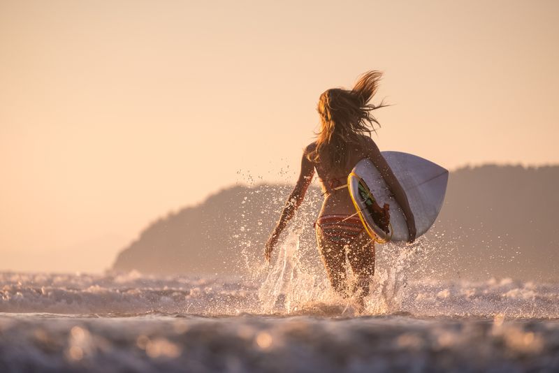 Girl walking on hte ocean sure with a surfboard