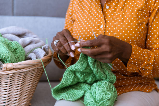 View from the front of a Black womans hands knitting, using green yarn. 