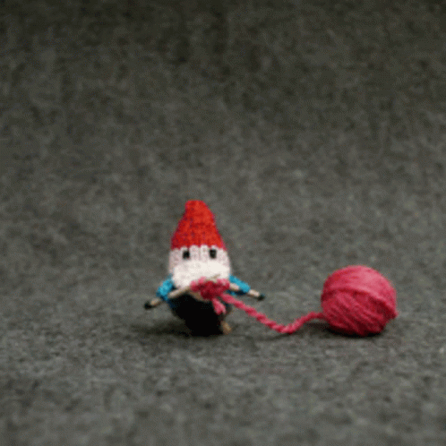 GIF of a knitted gnome knitting a heart, which floats up and away off the top of the page.
