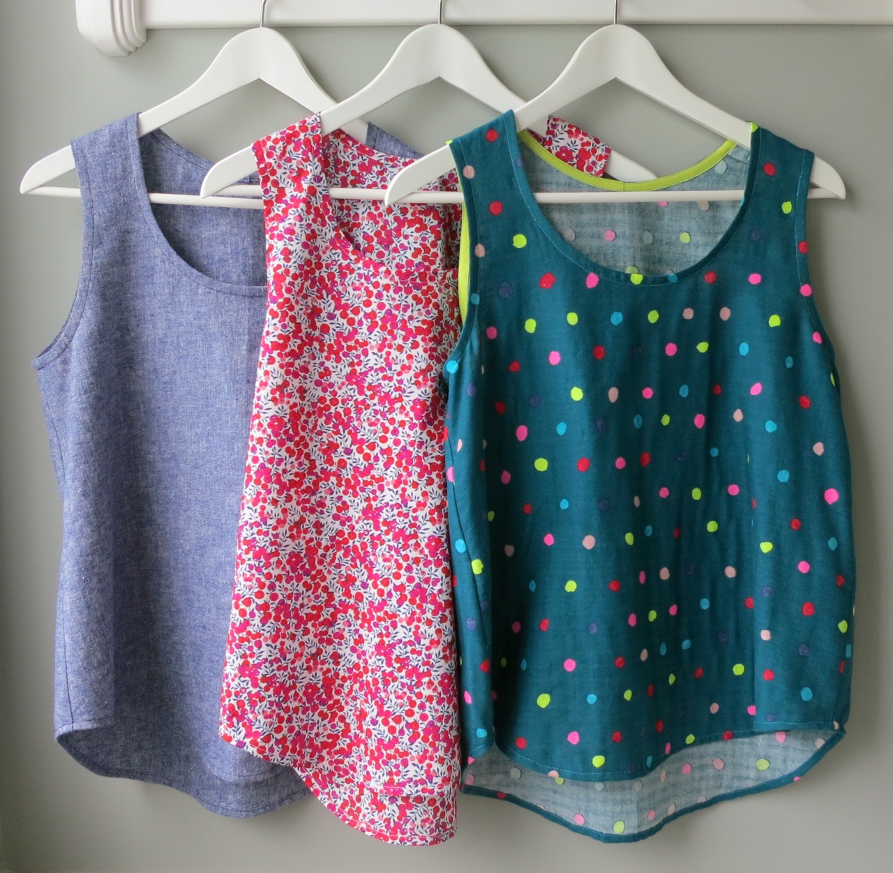 Two colourful box shaped tanktops are hung up against a white wall