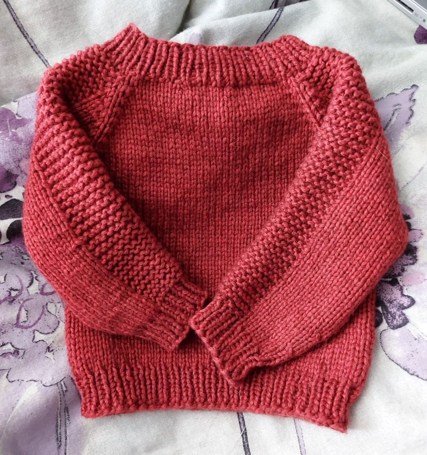 A knitted red-orange baby sweater