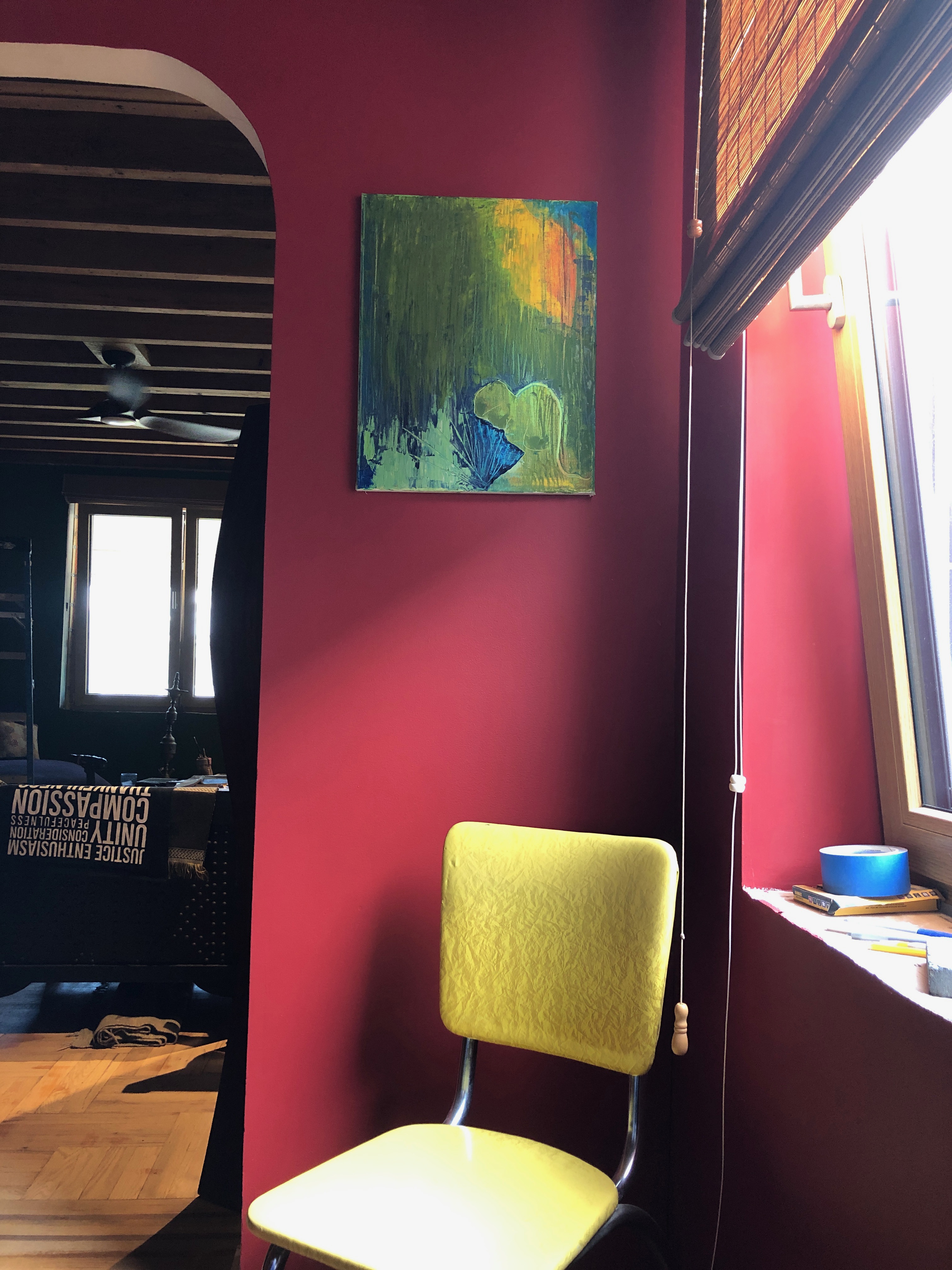 Photograph of a light-filled room with walls painted red. A yellow chair is placed in the corner. Above the chair is an abstract 
      painting with bright greens, turquoise and yellows