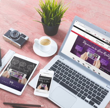 This is of an image of an Iphone, macbook air, ipad, coffee, a plant and a camera sitting on a pink wooden surface.