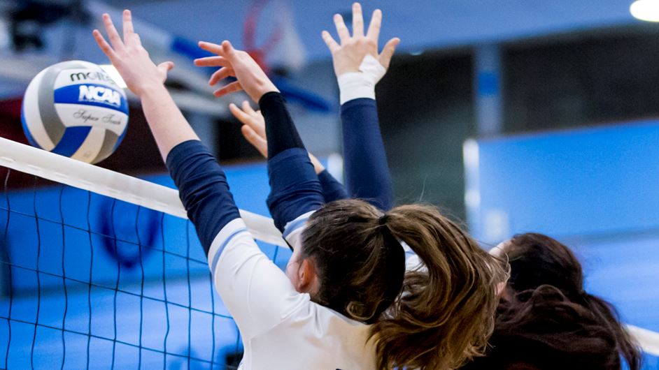 Two female volleyball players blocking the ball at the net