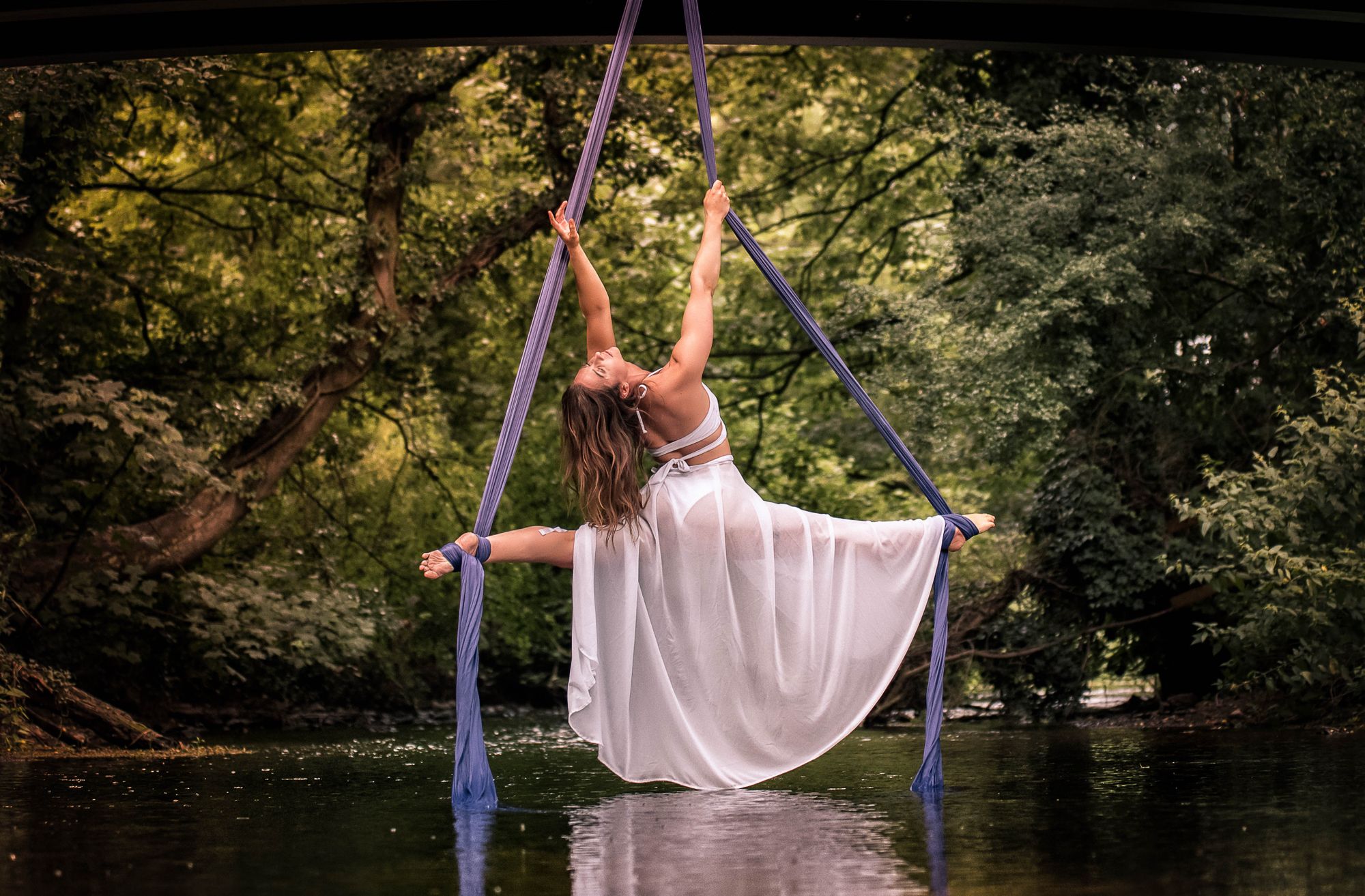 Woman performing aerial silks over a lake