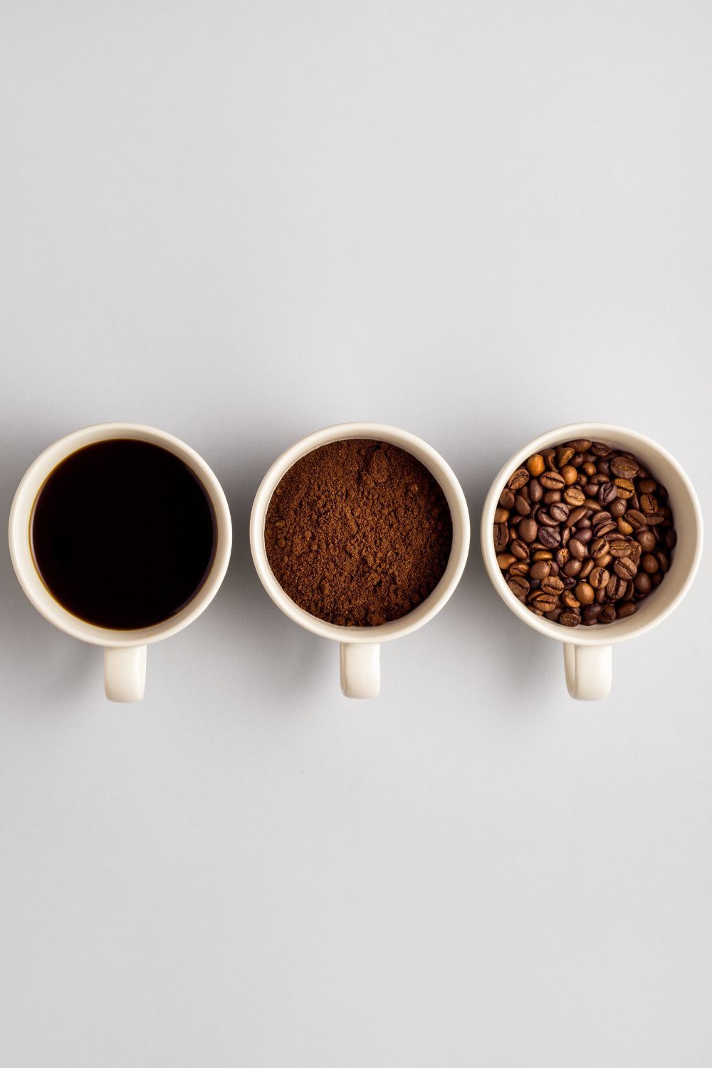 Left to right: cup of brewed coffee, cup of coffee bean grinds, cup of whole coffee beans