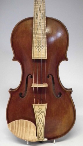 A baroque violin against a gray backdrop. It has a short fingerboard, which is a light colour and decorated with patterns like the tailpiece. Its gut strings are visible against the dark wood of the instrument.