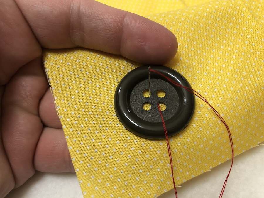 Button being sewed on a yellow fabric