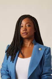 A Black woman with long hair wearing a blue blazer over a white
      shirt