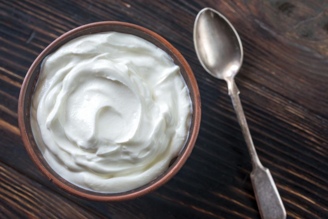 greek yoghurt in a brown bowl on a wooden table with a silver spoon on a side