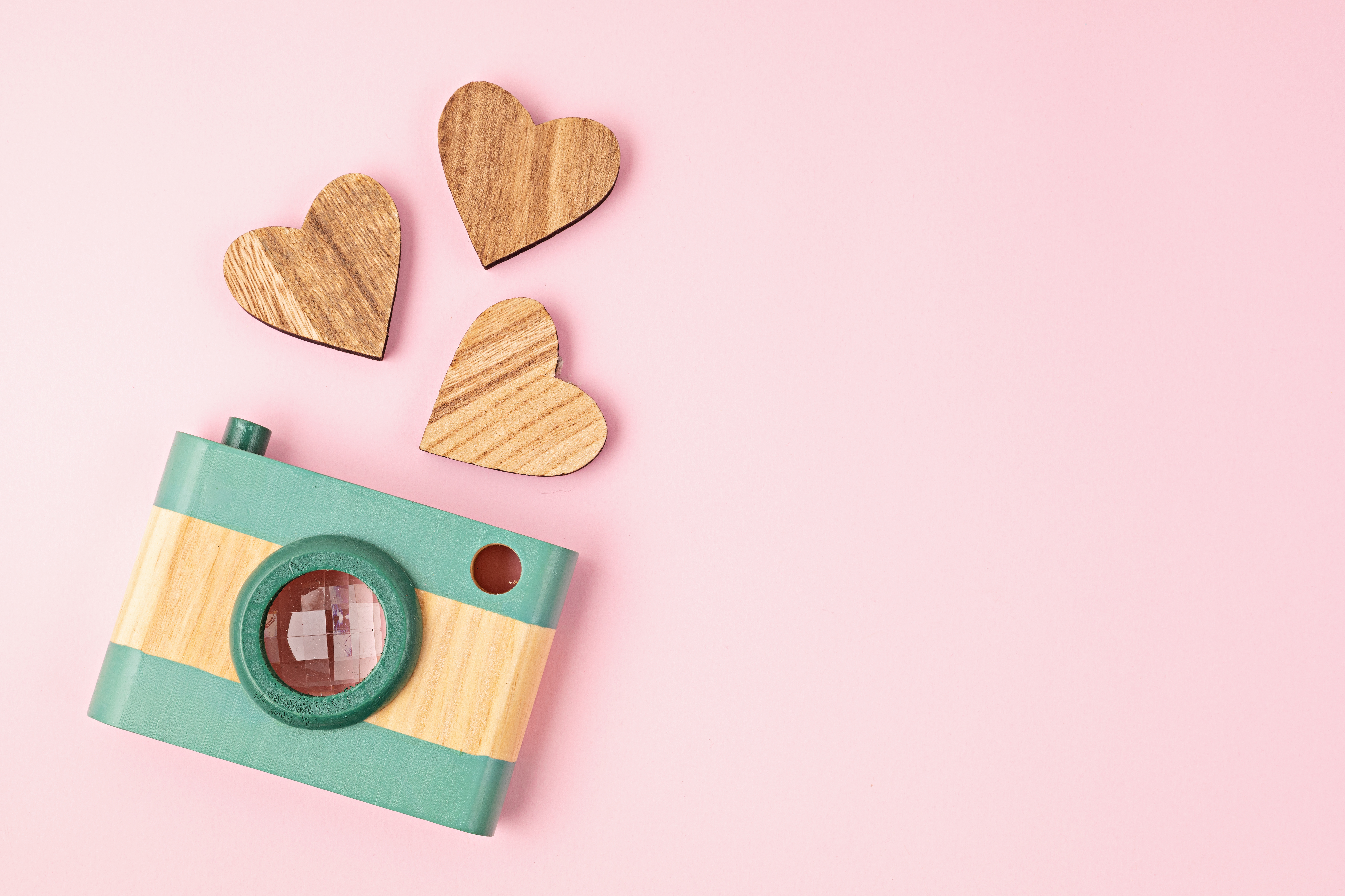 wooden camera with three wooden hearts on pink background