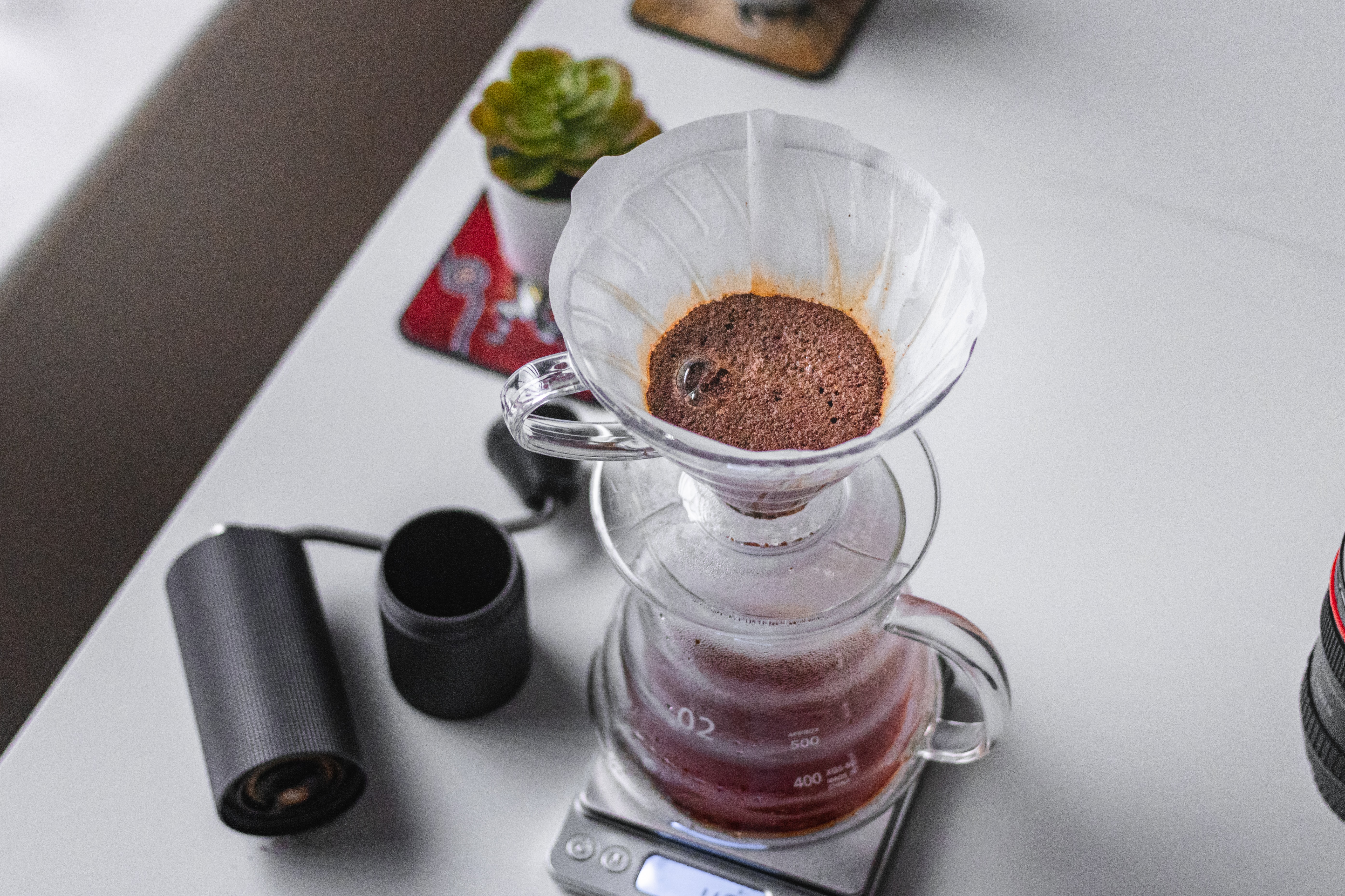A pourover coffee setup on a kitchen scale, with a black hand grinder. Photo by Pradeep Javedar on Unsplash.