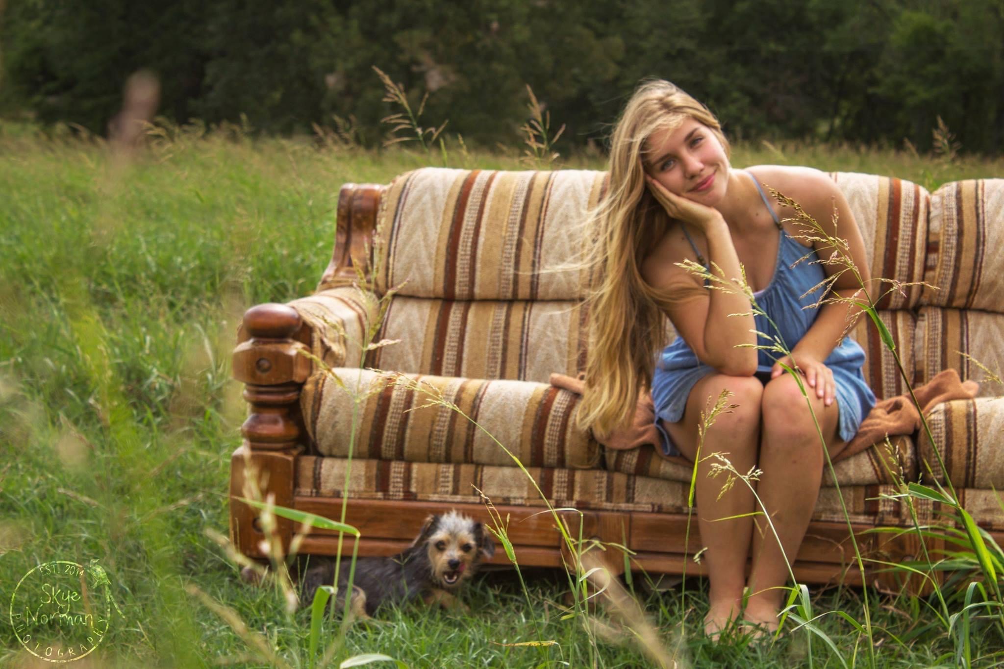 girl smiling with head resting on palm and sitting on couch in a field