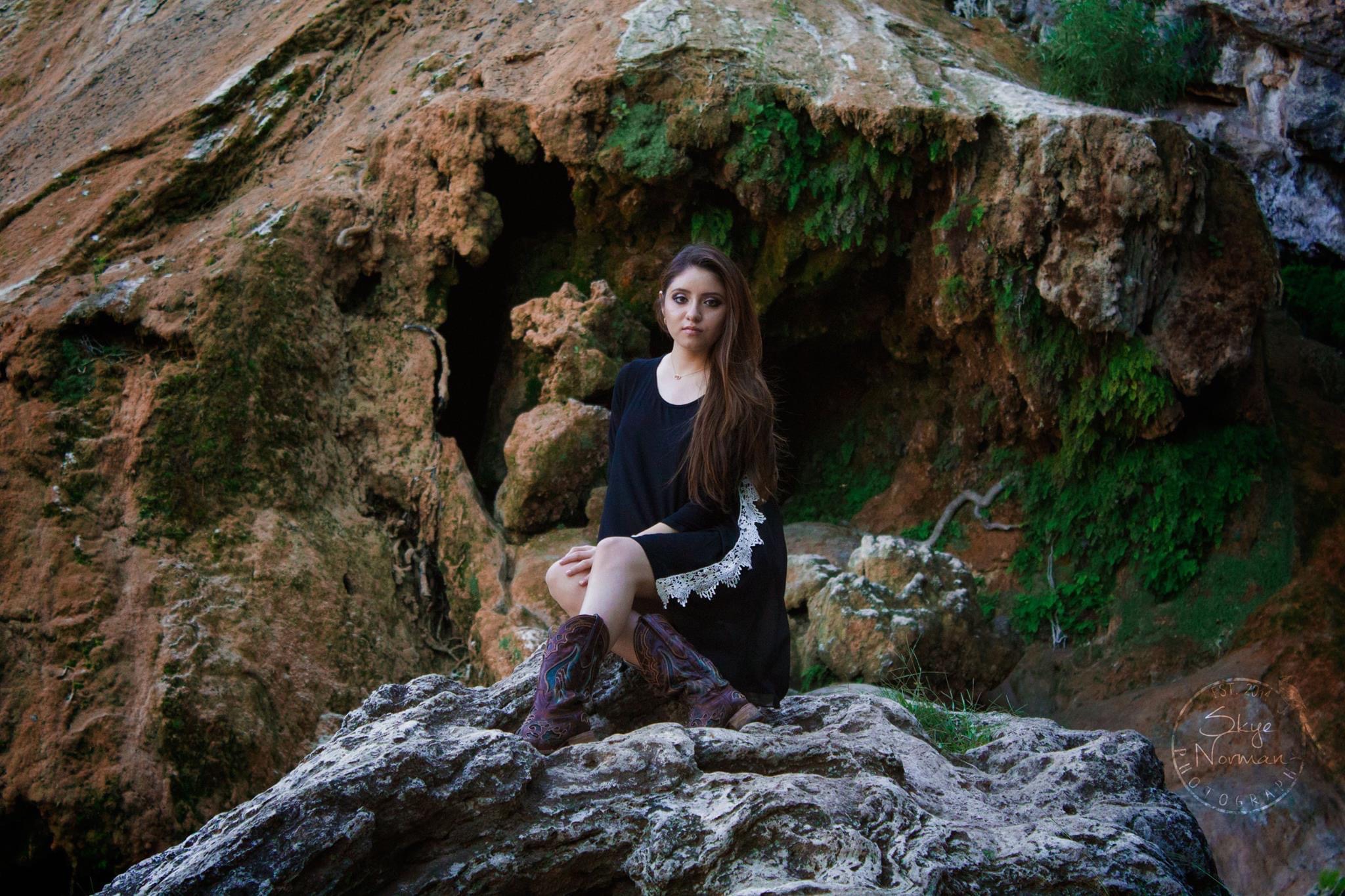 girl sitting on large rock formation with crossed legs and a stoic expression