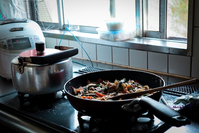 A pan on a stove holding a delicious meal and a spoon used to stir the ingredients