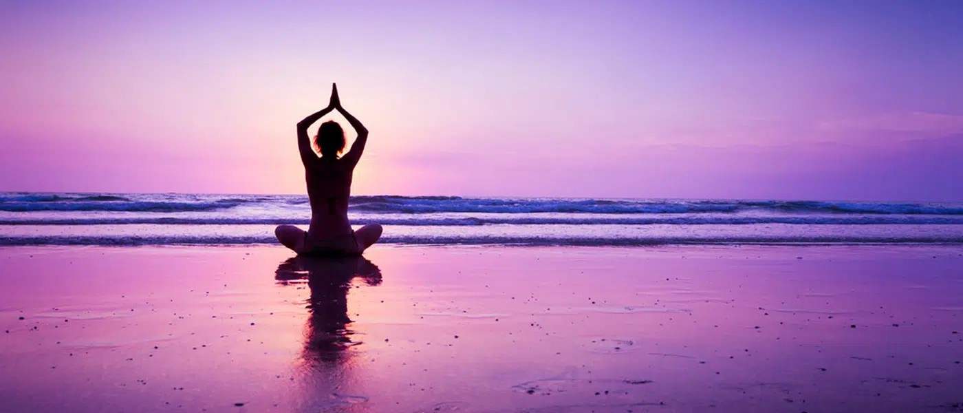 Person in a seated yoga pose at sunset on a beach in front of waves coming in