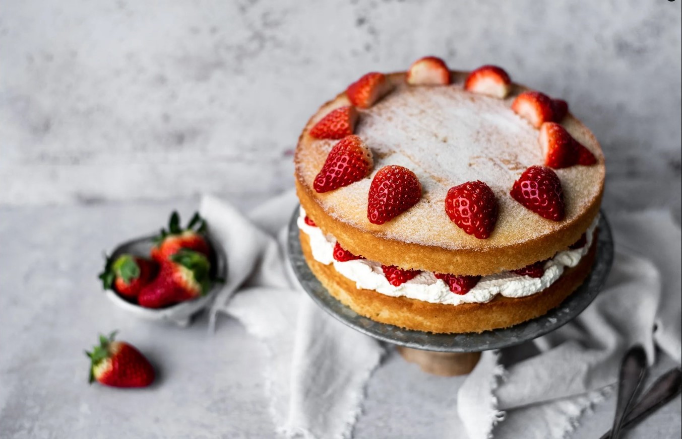 A Victoria sponge cake with straweberries that have been cut in halves on top.