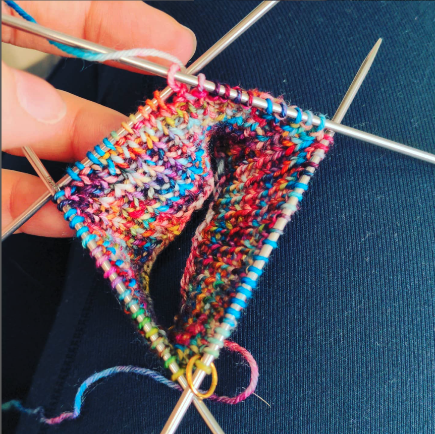 close up of four double-pointed knitting needles with brightly colored rainbow yarn