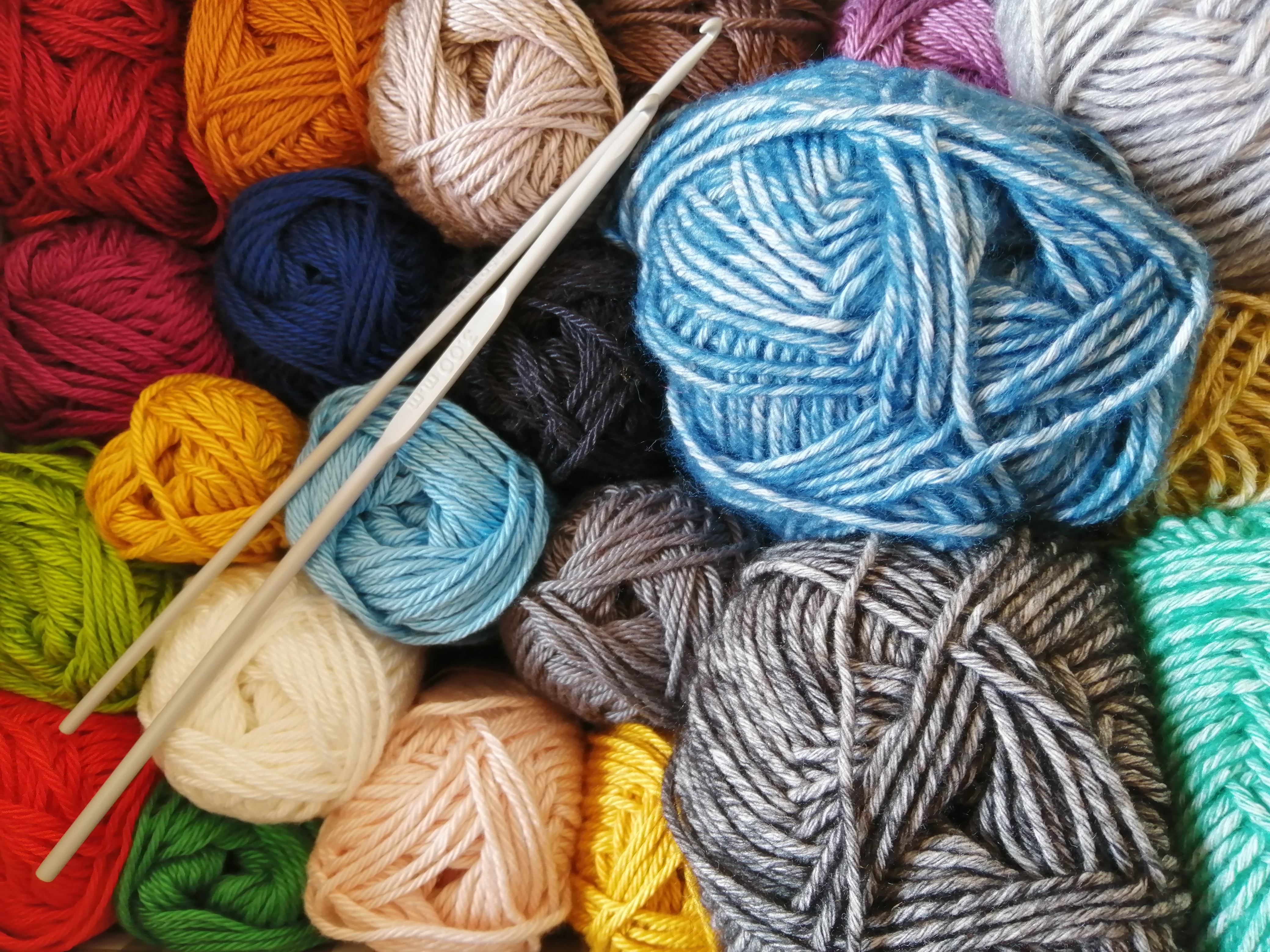 several skeins of yarn in various colors with a pair of knitting needles sitting on top of them