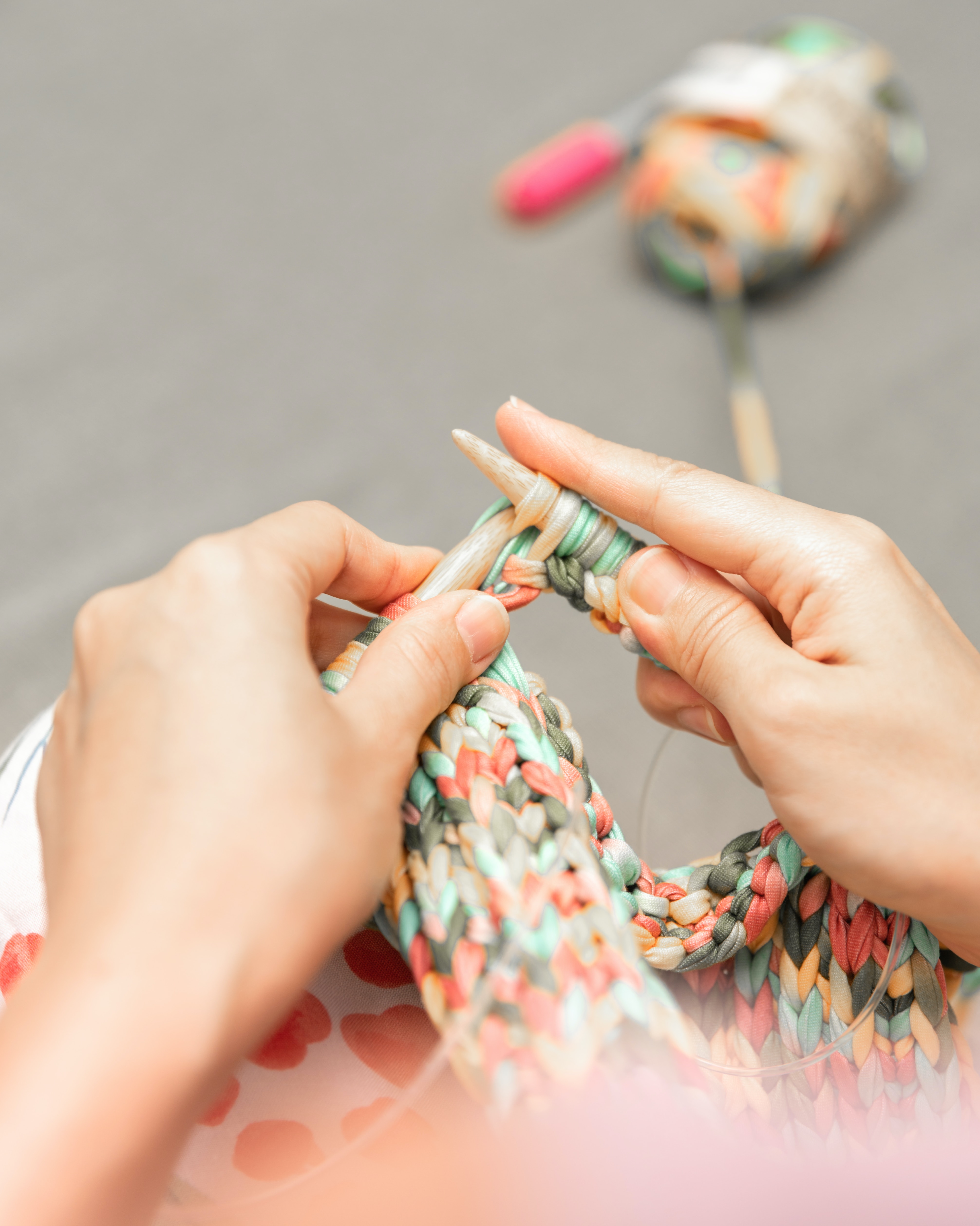 close up of hands knitting a project with a variegated yard of peach tree colors ranging from peachy pinks to leafy greens