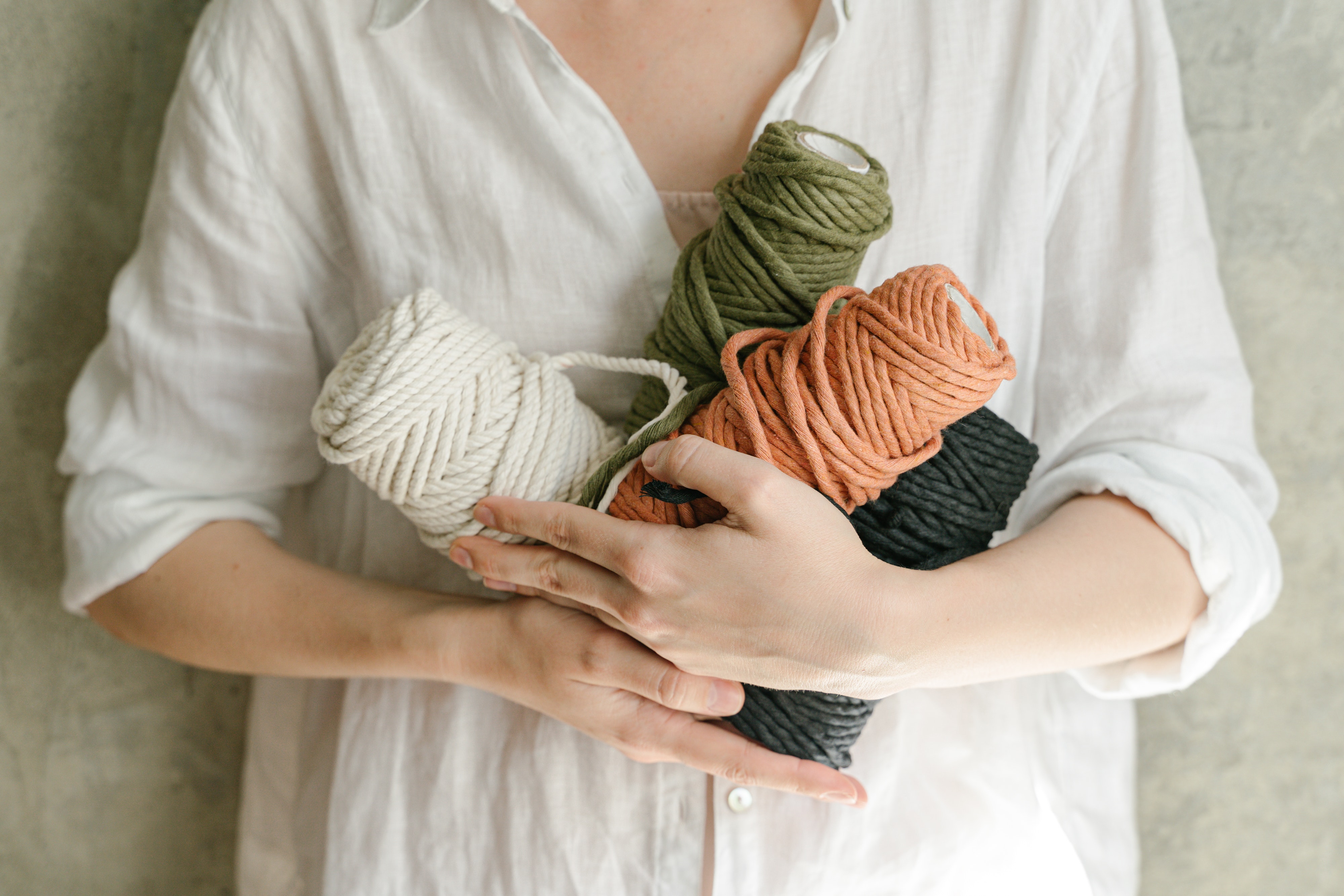 white woman in a white linen shirt holding four skeins of yarn