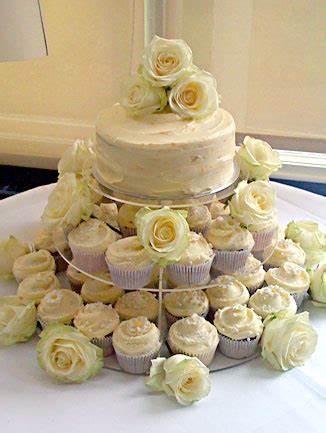  white wedding cake on stand surrounded by cupcakes