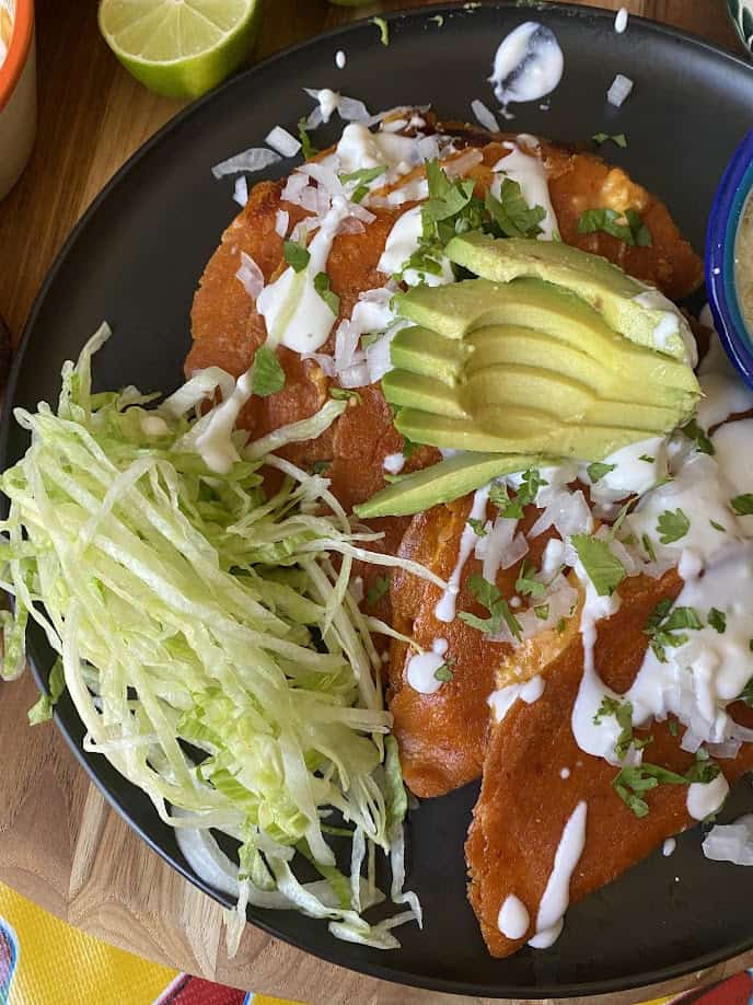 Enchiladas potosinas filled in with fresh cheese, panela chesse and salsa; on top of it has slices of onions, cilantro, cream cheese, salsa, refried beans and rice. Enchiladas potosinas rellenadas con queso fresco, queso panela, y salsa; acompañado con cebolla, cilantro, crema, una salsa picosa, frijoles refritos y arroz. 