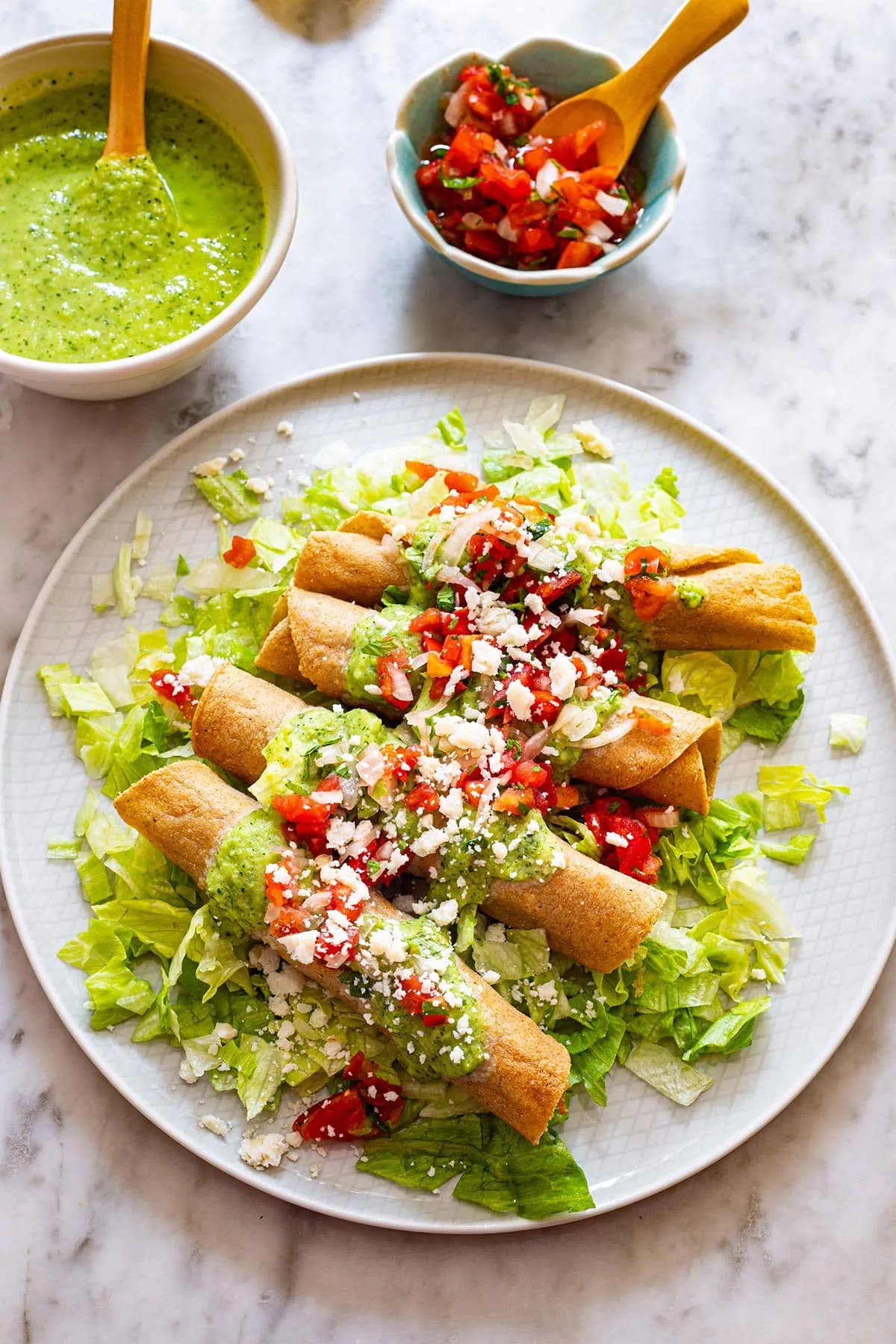 Flautas de pollo con salsa de tomatillo y serrano, pico de gallo, lechuga y queso fresco.